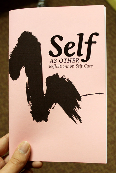 a photo of the Self As Other zine, featuring a plain peach cover with a black swoosh of ink and the title in black.